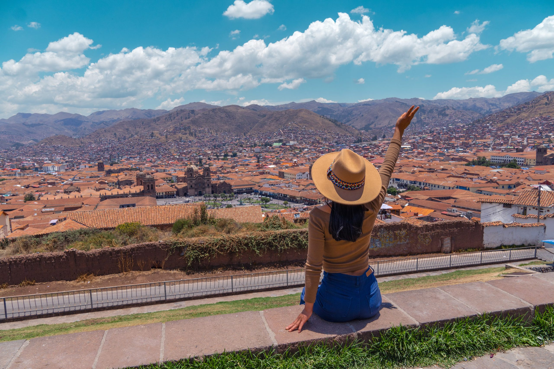 Happy Latin tourist woman sitting watching the Plaza de Armas in Cusco from the viewpoint.