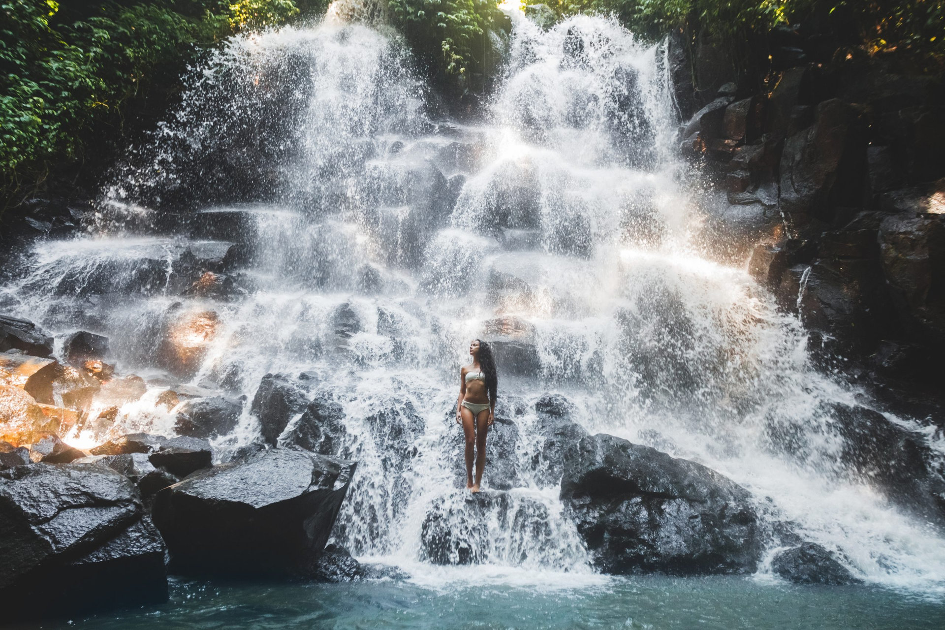 Woman enjoying under stream of big and beautiful cascade waterfall. Girl with slim body and long hair. Kanto Lampo in Ubud area