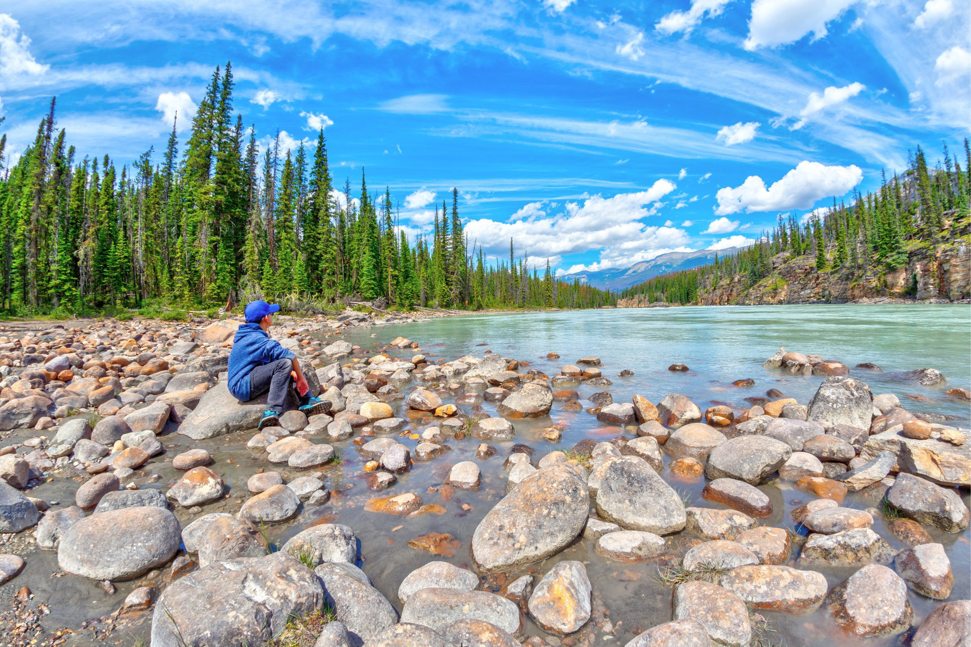 A boy sits on the edge of the Athabasca River resting and enjoying the tranquility in nature of the Canadian Rockies at Jasper National Park in Alberta.