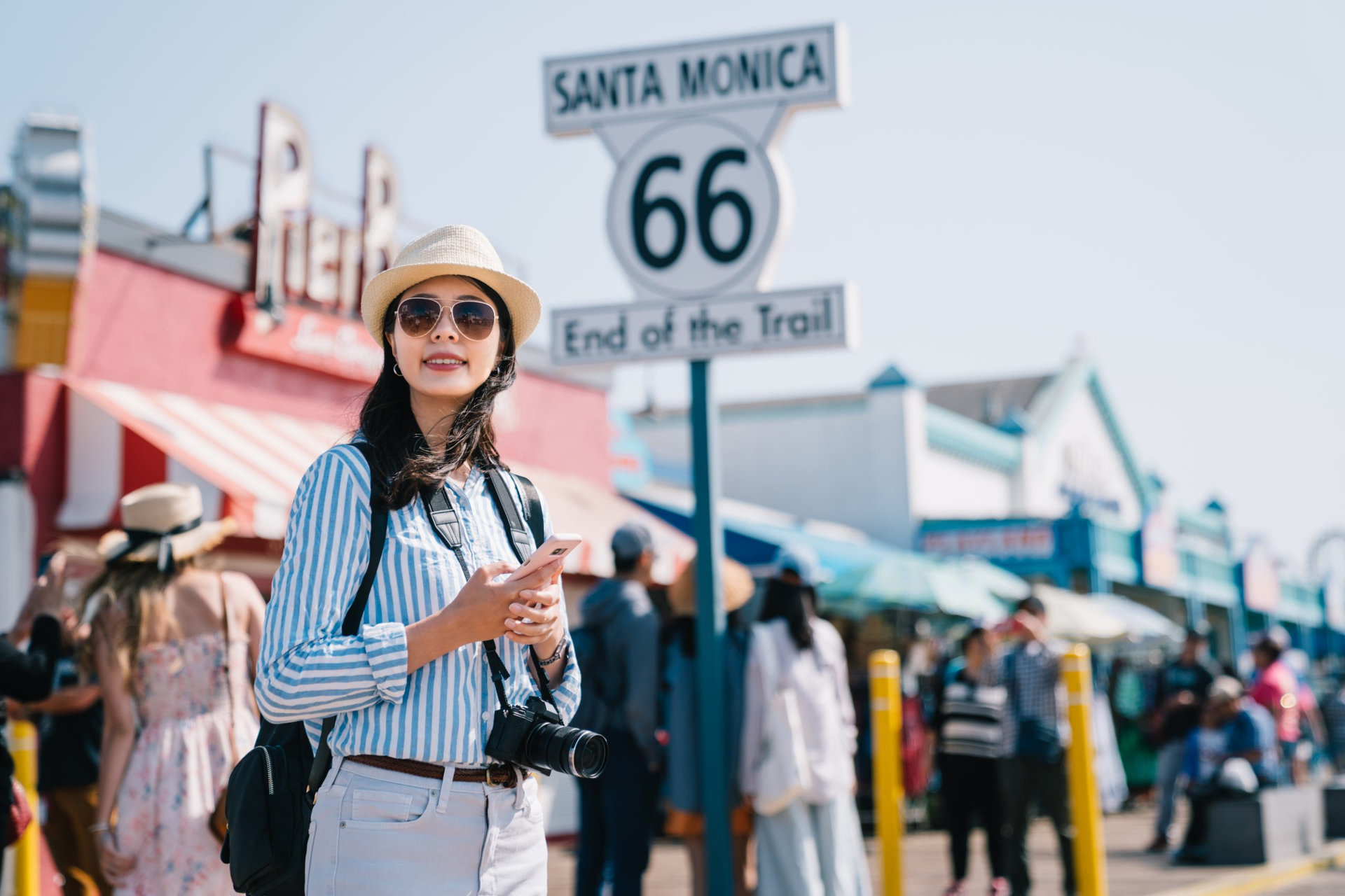 an elegant female tourist using cellphone checking the map, standing next to the sign of Santa Monica