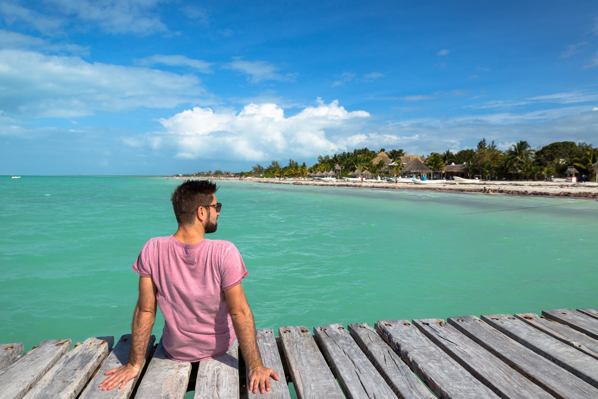 Young male sitting at wooden pier and looking to the sea