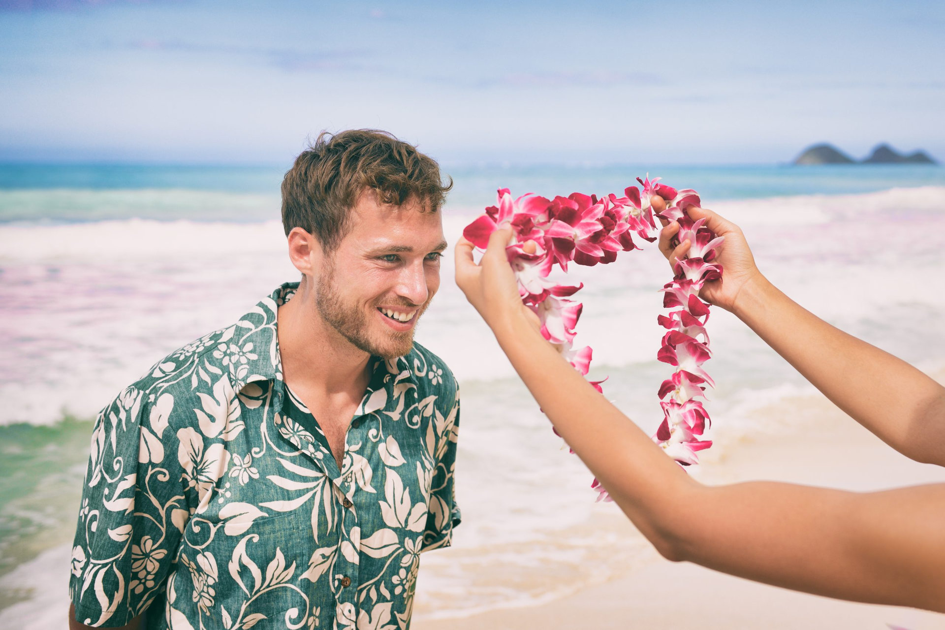 Hawaiian lei flower garland necklace welcome gesture of giving orchids welcoming tourist on Hawaii beach. Happy man receiving traditional gift on summer tropical holidays.