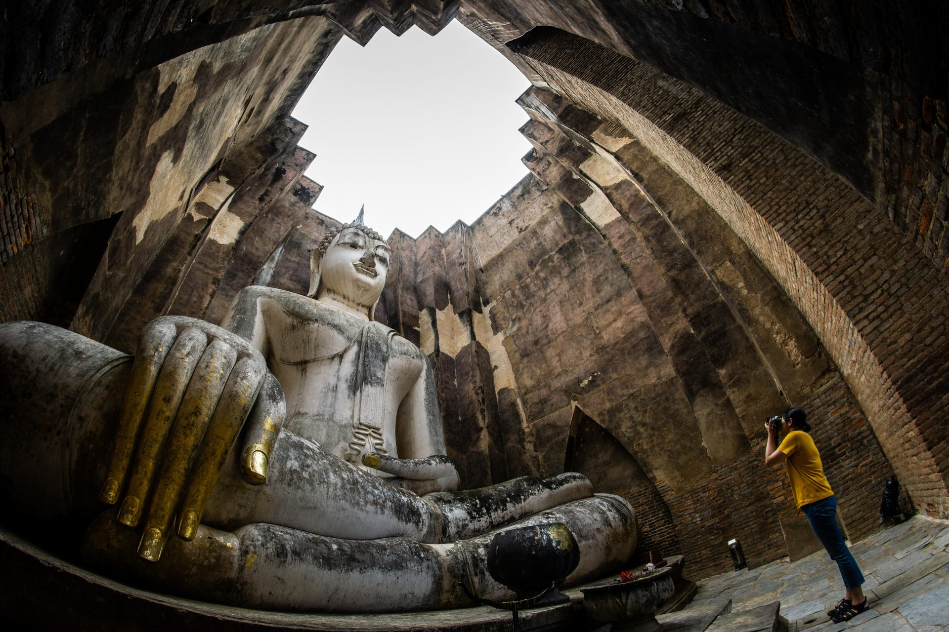 female traveler photographing temples at Sukothai historical park, Unesco world heritage, Thailand, the body to head part of the big buddha image at Wat Sri Chum in Sukhothai.