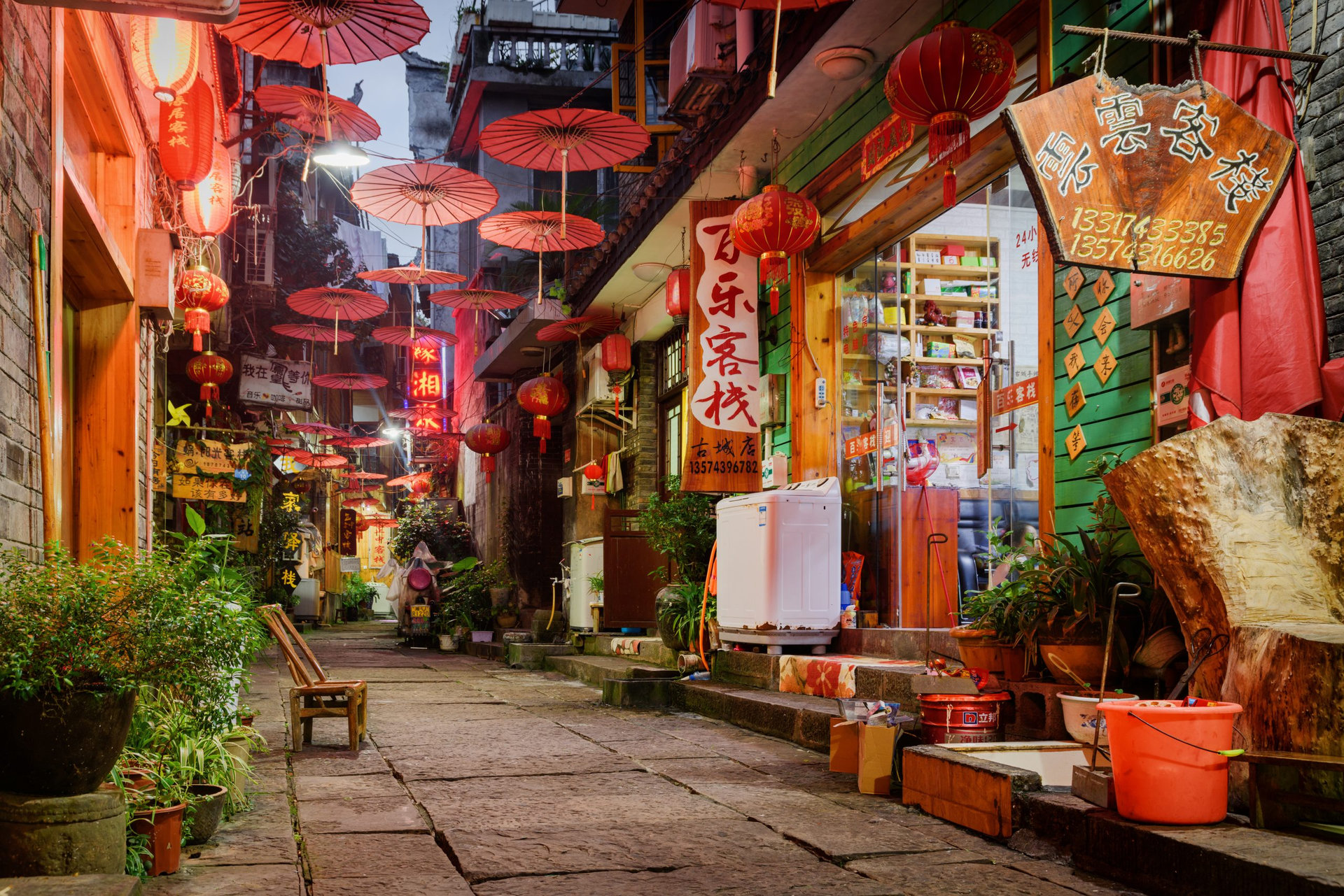 Fenghuang, China - September 22, 2017: Wonderful view of scenic narrow street decorated with traditional oriental Chinese red umbrellas in Phoenix Ancient Town (Fenghuang County) at evening.