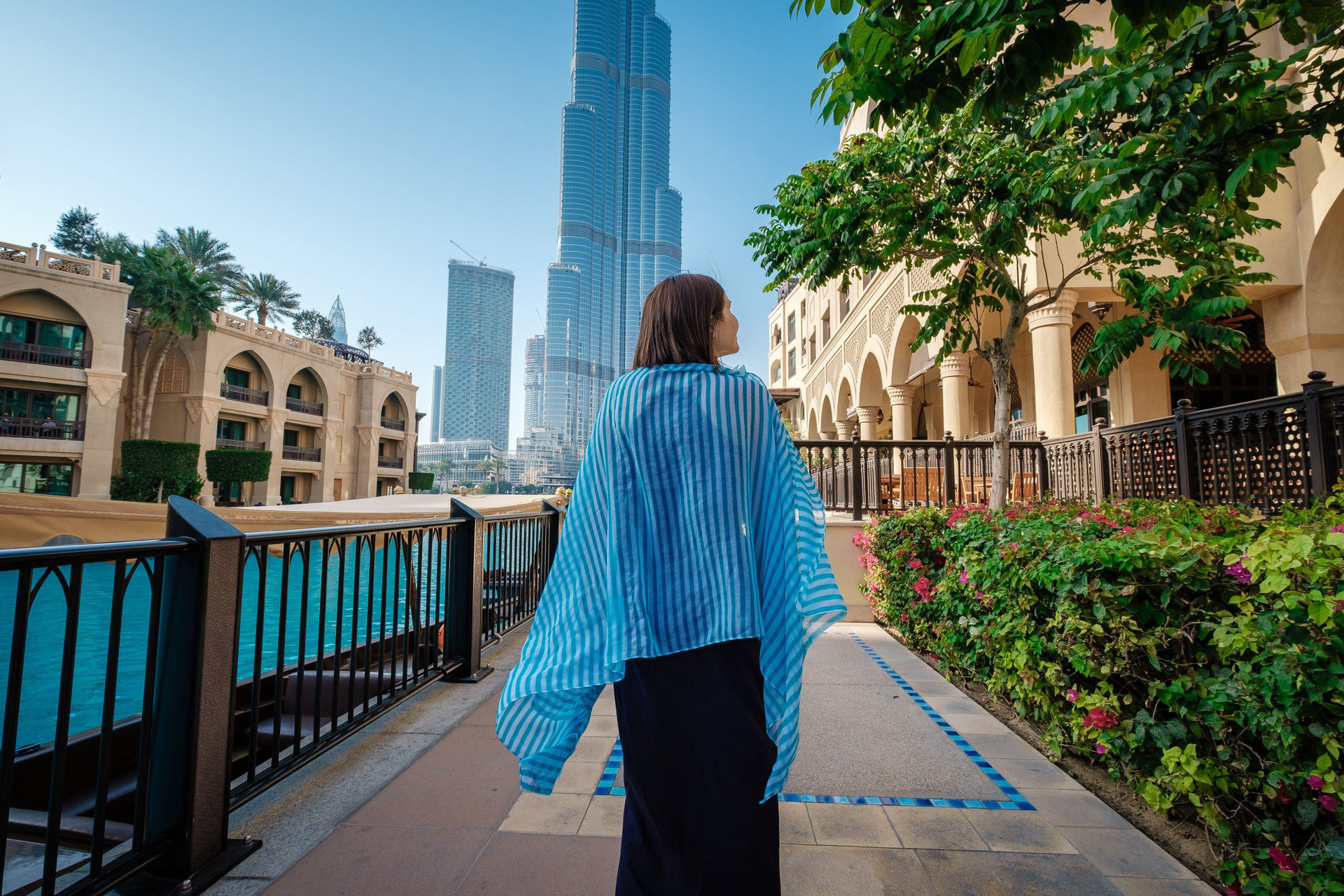 Enjoying travel in United Arabian Emirates. Young woman in dress walking on Dubai Downtown. Back view of pretty woman on the walk