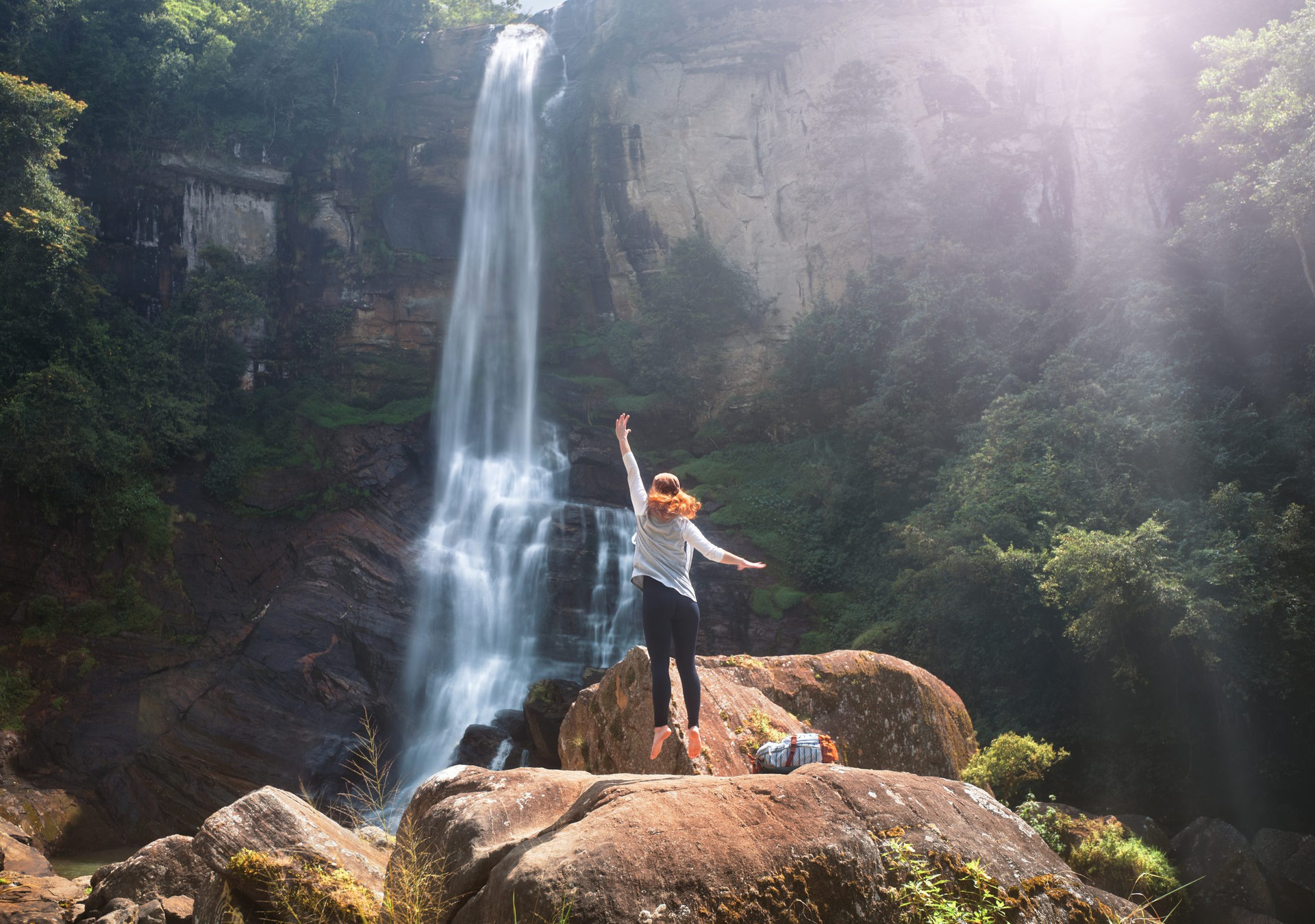 Young woman traveler is having fun on summer vacation on the background of Ramboda waterfall on the island of Sri Lanka. Concept travel in Asia, emotion and fun
