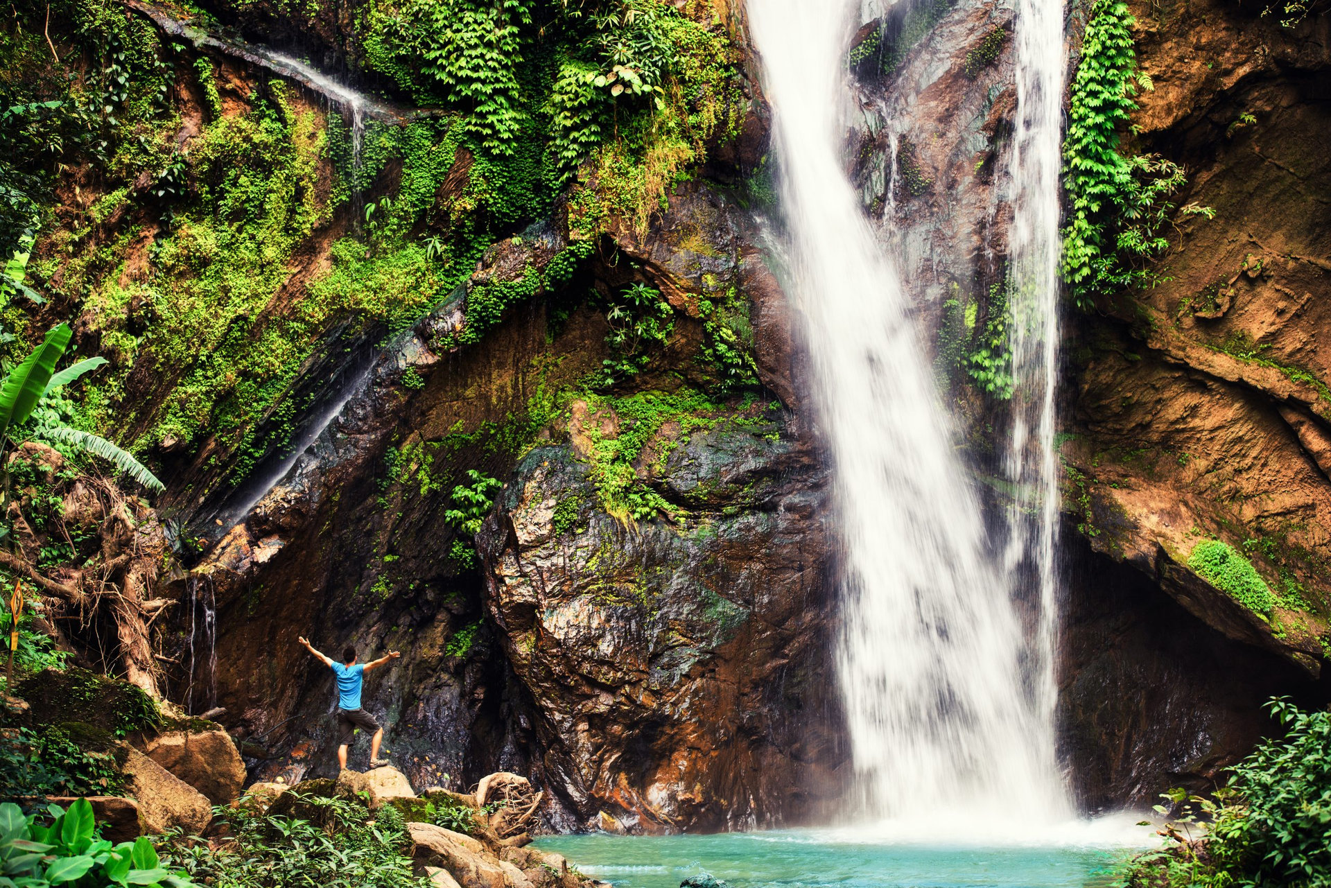 Hiker standing in front of huge Jungle waterfall surrounded by lush Jungle vegetation and flora in Bali, Indonesia