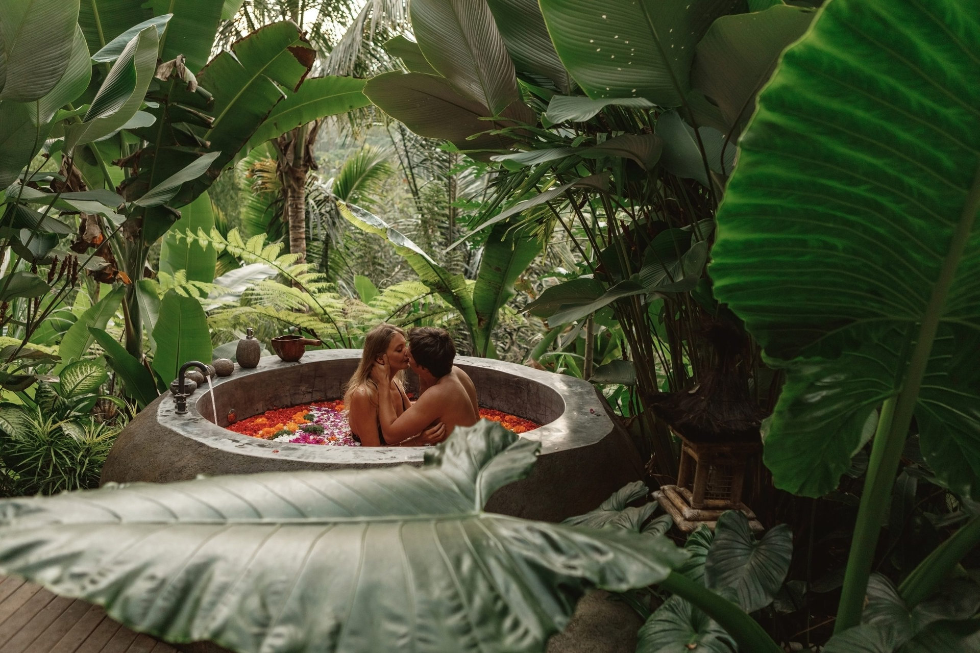 Beautiful couple resting in hotel spa. Woman and man relaxing in bath with tropical flowers outdoor at luxury hotel resort in the jungle