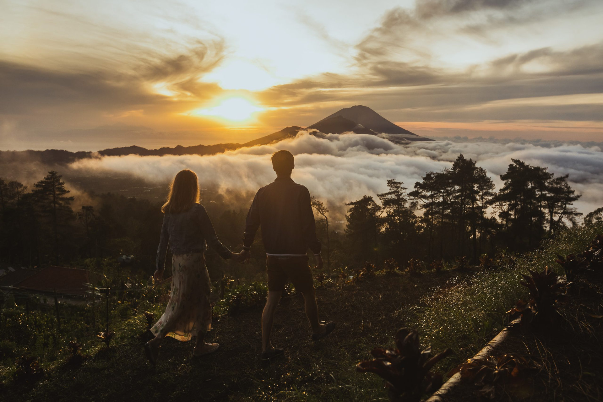 A loving couple man and woman walking near Batur volcano. Back view. Hold hands. Sunrise. Sunset. Tourists lovers on honeymoon enjoying summer vacation. Travel bloggers. Bali landmark
