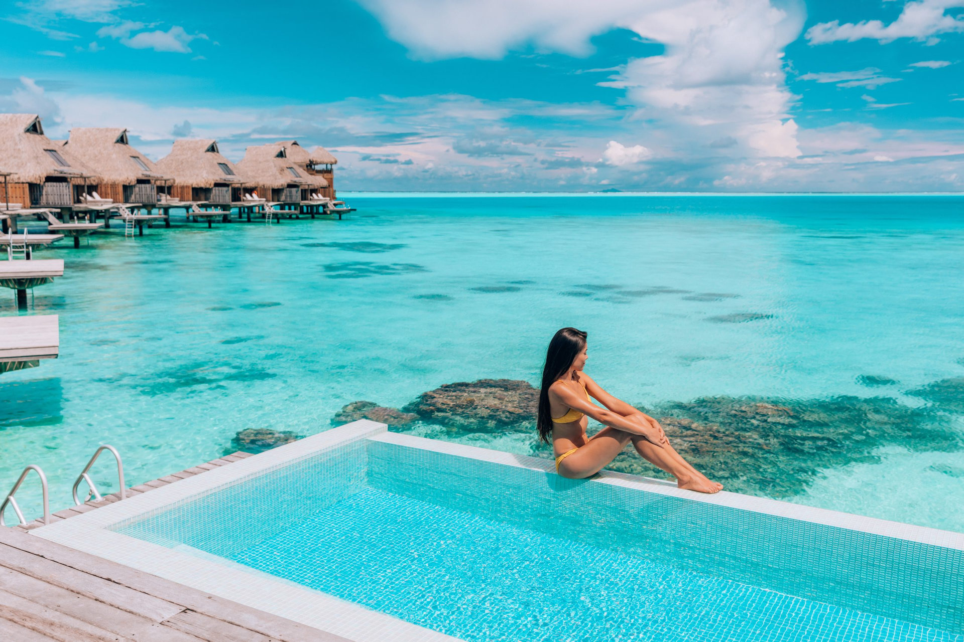 Luxury resort travel vacation destination idyllic overater bungalow villa woman relaxing by infinity pool. Social media influencer traveler luxurious high end lifestyle.