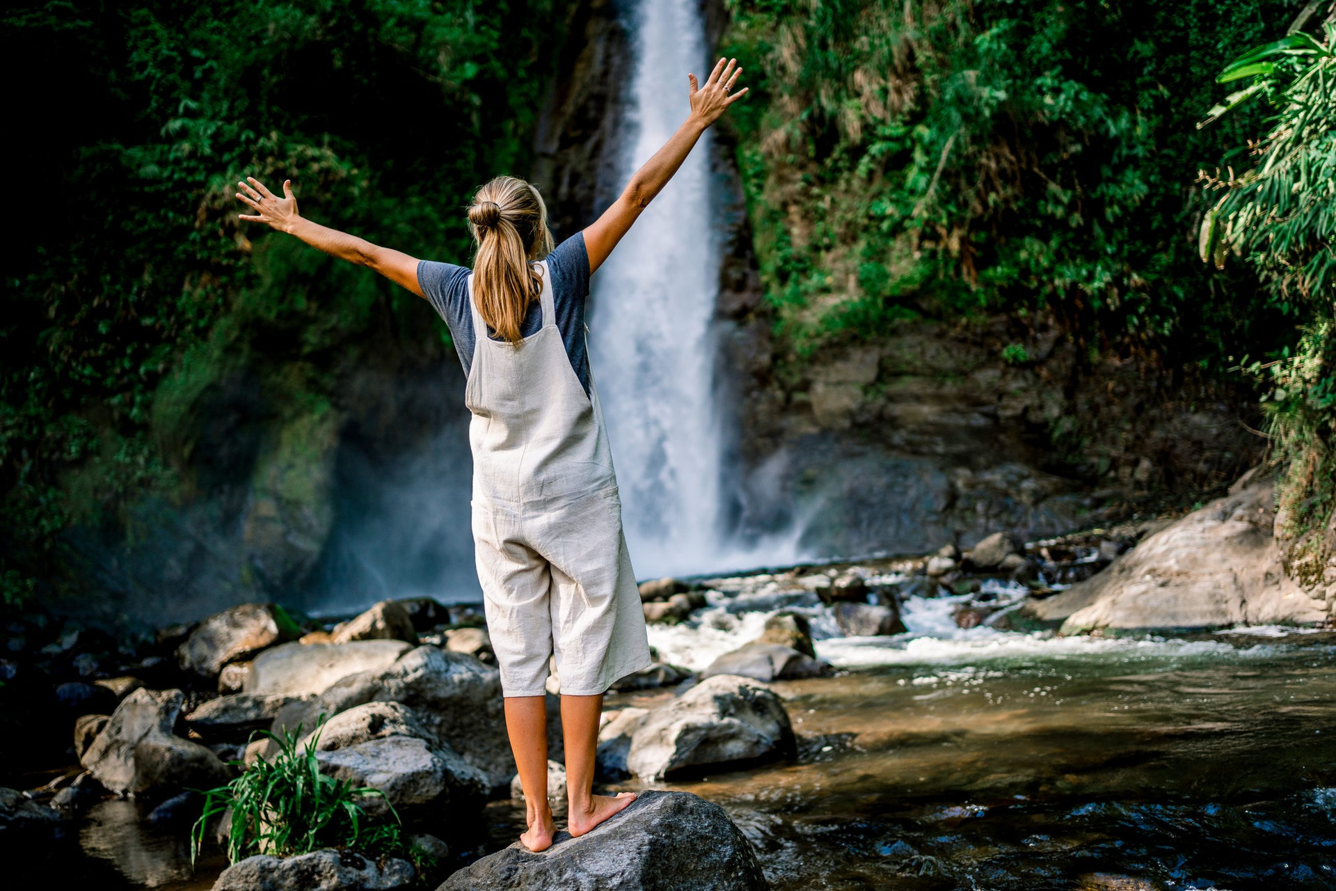 Young woman raising her hands as a freedom gesture facing a waterfall in the middle of the jungle