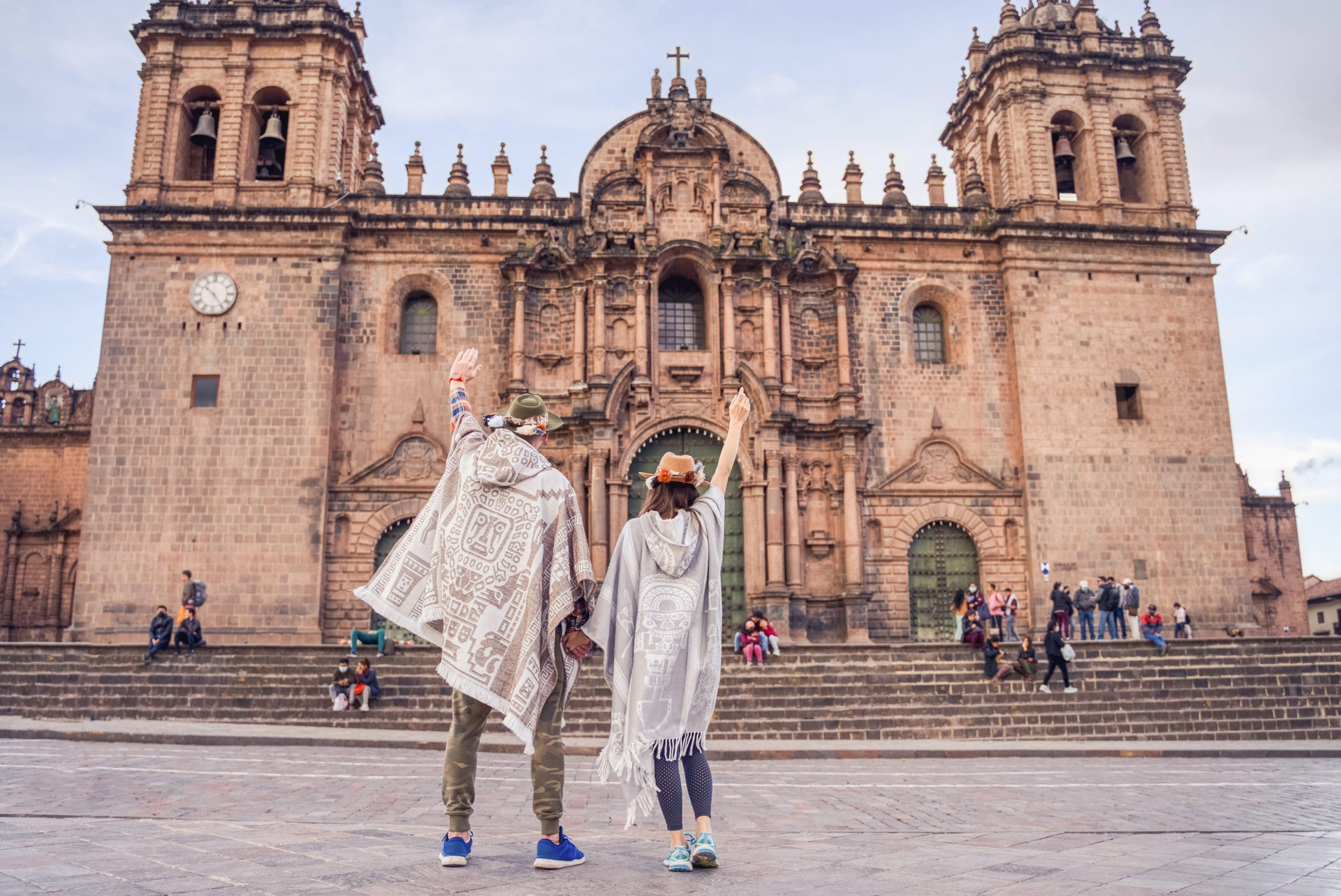 tourist couple celebrating in front of the cathedral in the main square of cuzco wearing sombreros and ruanas