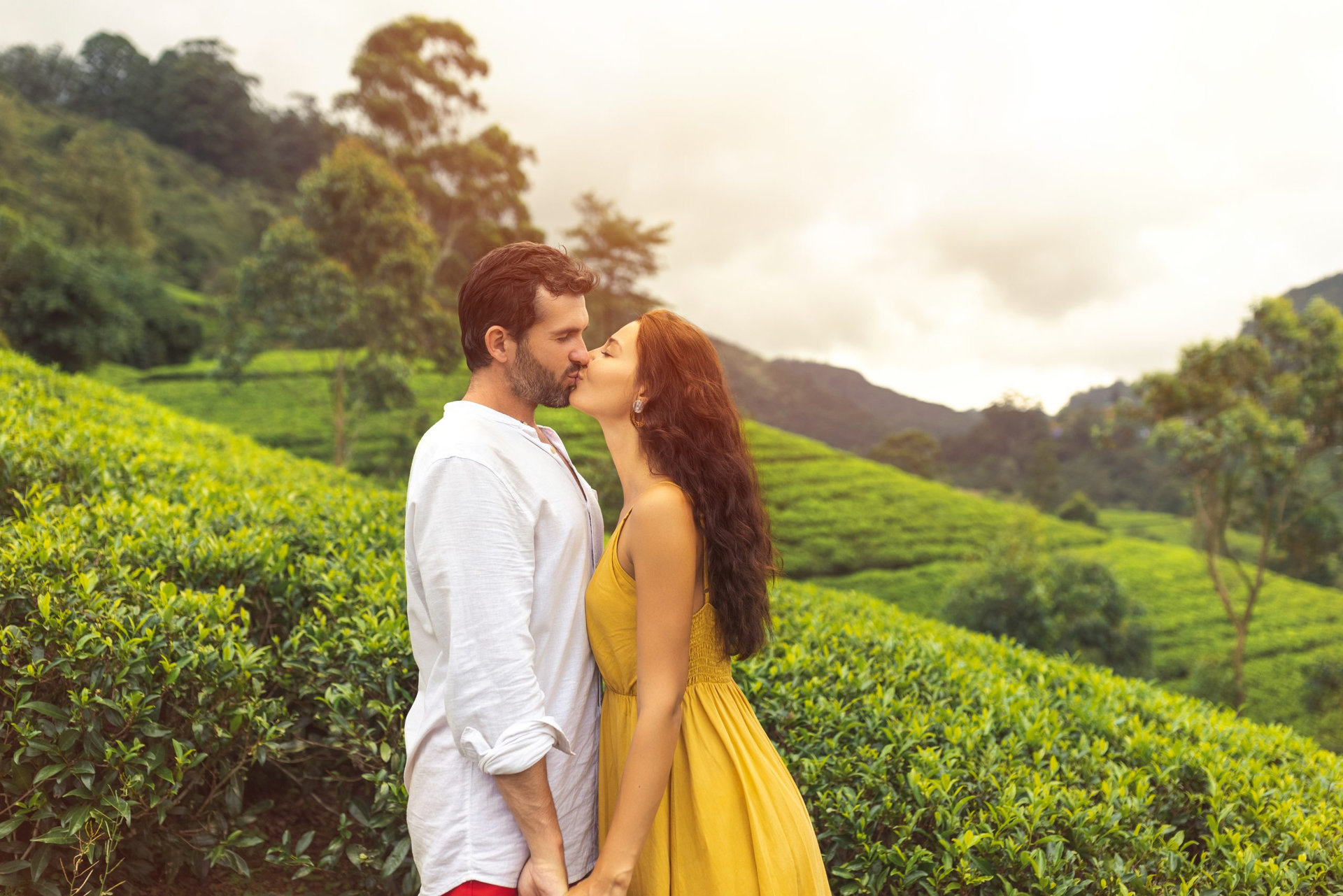Romantic couple of travelers in love kissing against nature background tea plantations landscape. Young adult brunette woman and man in front of perfect natural backdrop tea farm.