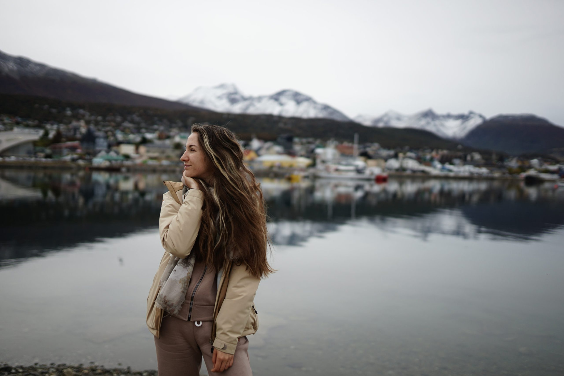 In the photo, a beautiful girl against the background of the city of Ushuaia, with houses of Argentine architecture and a beautiful view of the lake.