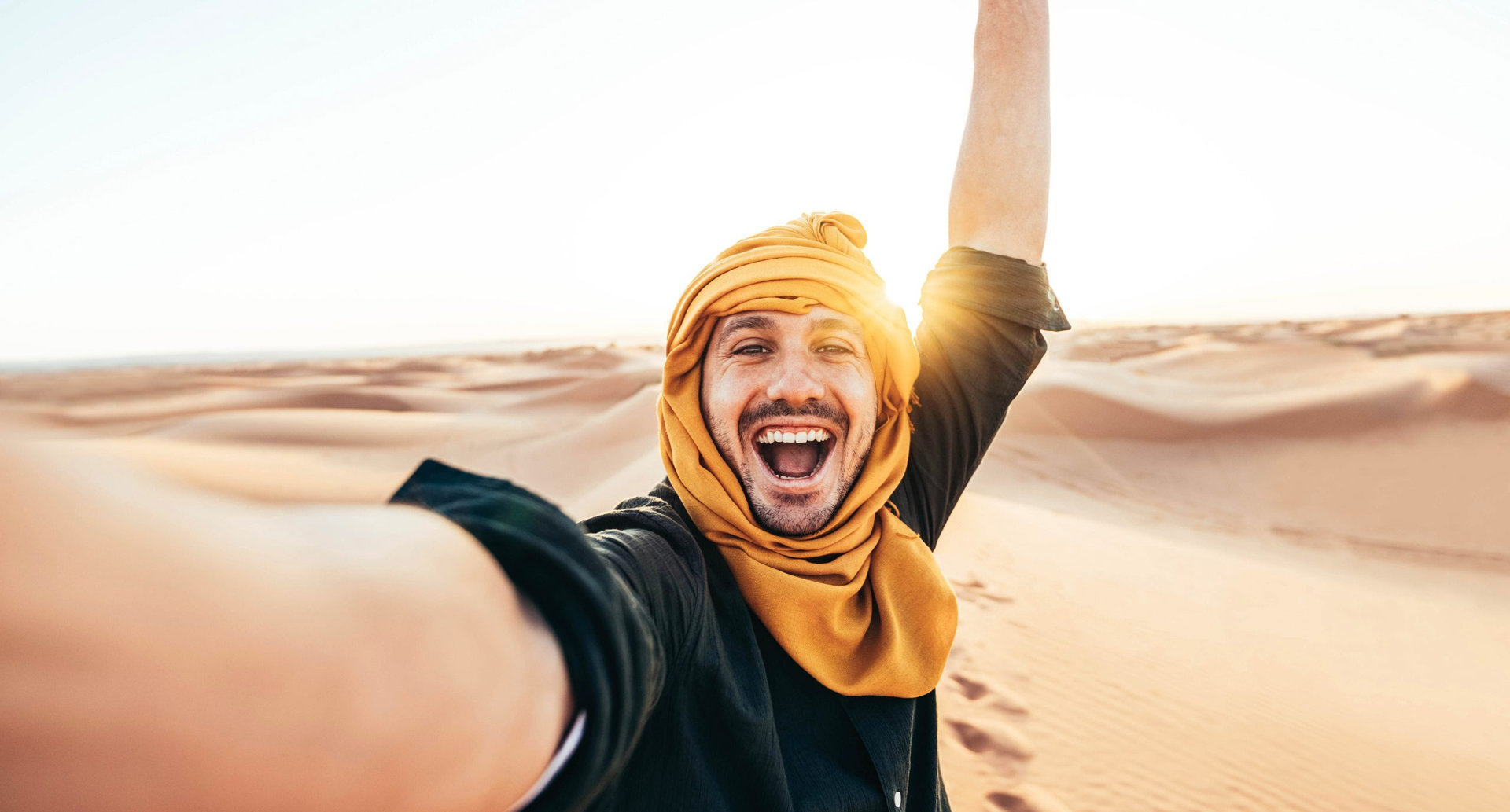 Happy male tourist taking selfie on sand dunes in the Africa desert, Sahara National Park - Influencer travel blogger enjoying trip while takes self portrait - Summer vacation and weekend activities