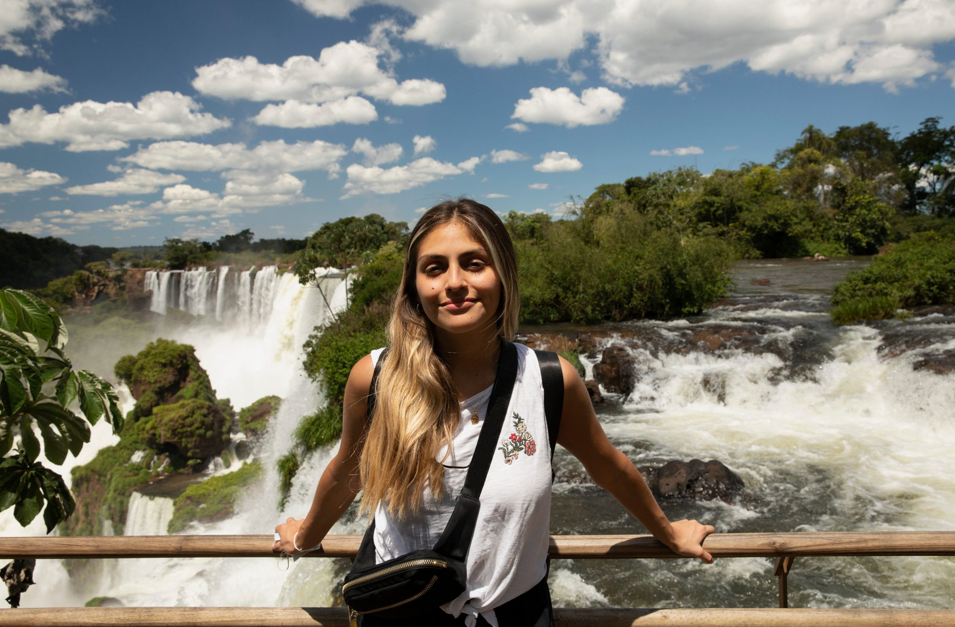 Tourism. Portrait of a young woman with brown hair smiling with the Iguazu waterfalls in the background.