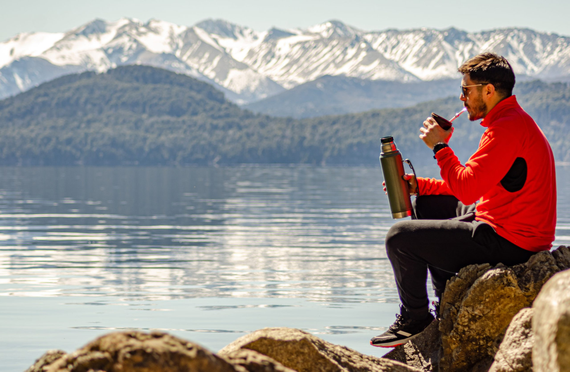 chico hombre persona a la orilla del lago rodeado de montañas tomando su mate argentino