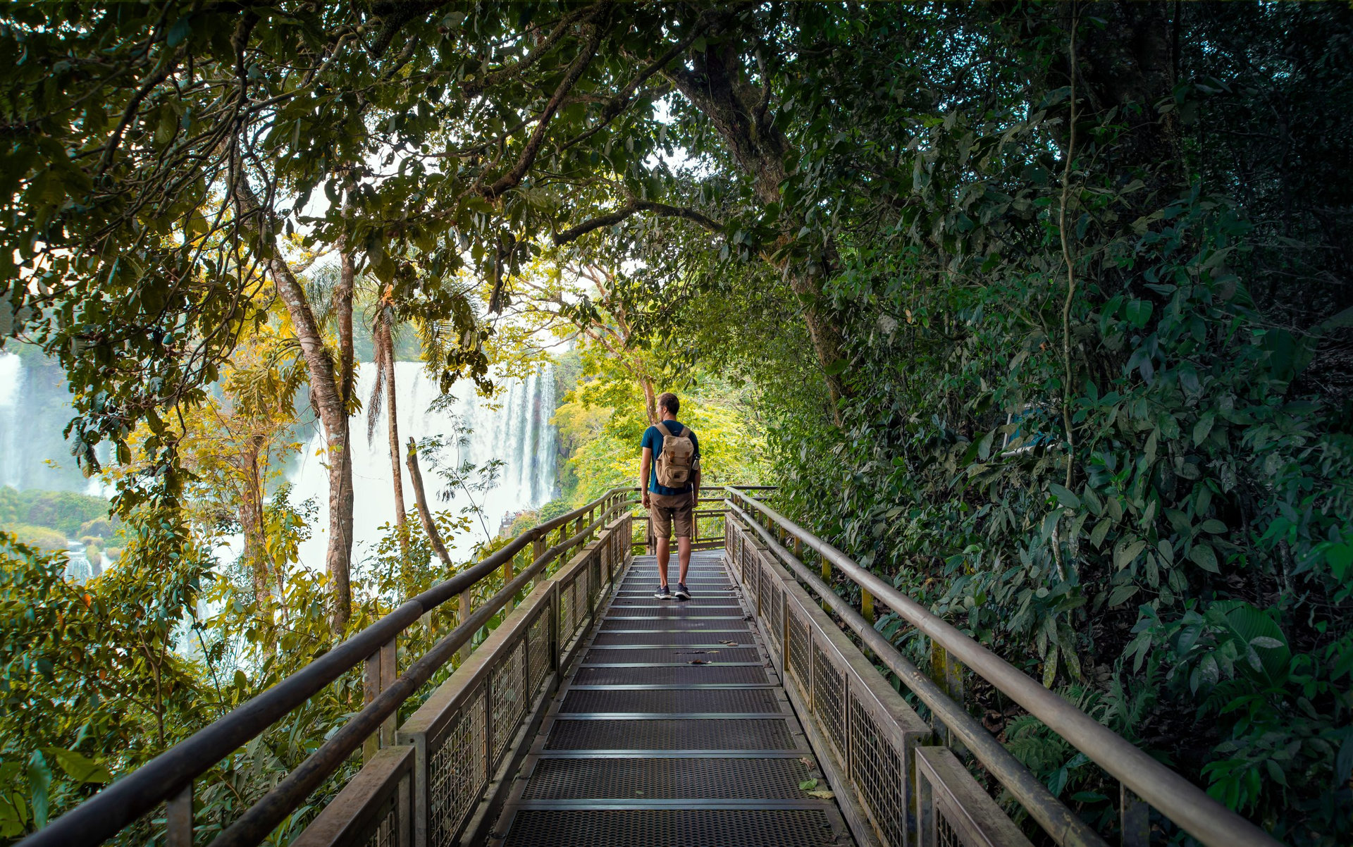 A man traveler with a backpack explores Iguazu Falls from the walkways in Argentina and Brazil