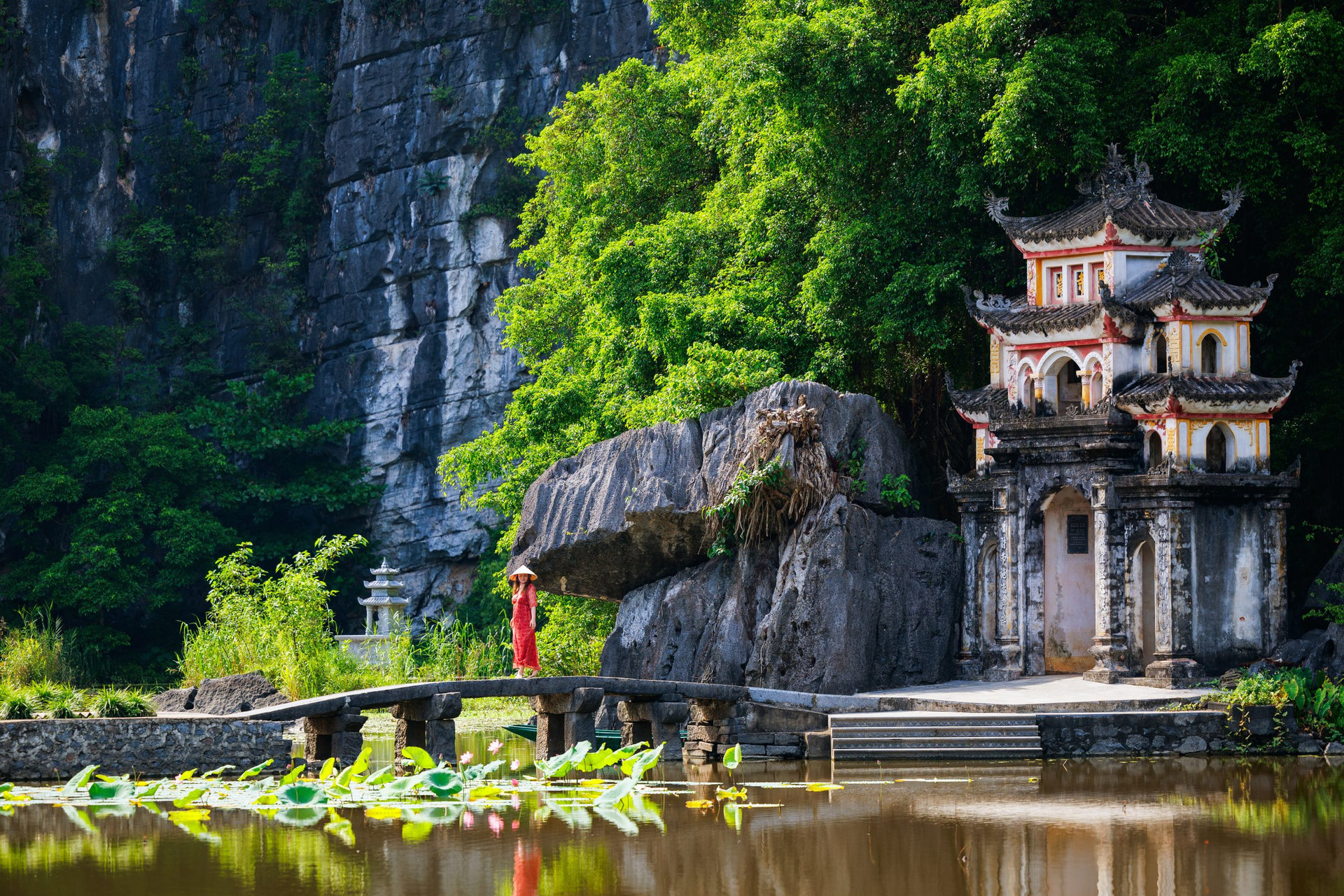Beautiful woman wearing red dress and conical hat visiting Bich Dong pagoda in Ninh Binh Vietnam. Bich Dong Pagoda is a popular tourist destination of Asia.