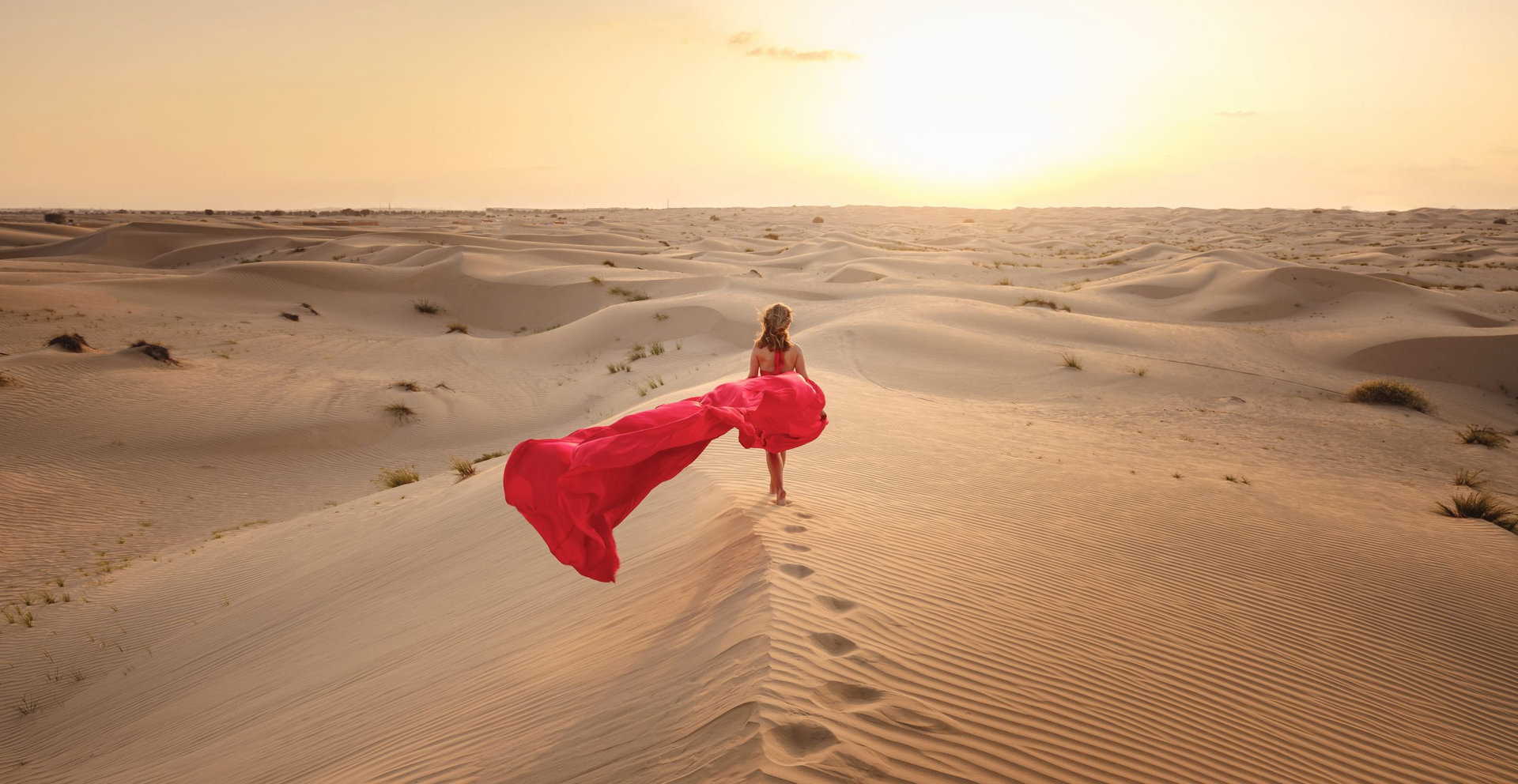 Desert adventure. Young arabian Woman in red silk dress in sands dunes of UAE desert at sunset, fantastic view. The Dubai Desert Conservation Reserve, United Arab Emirates.