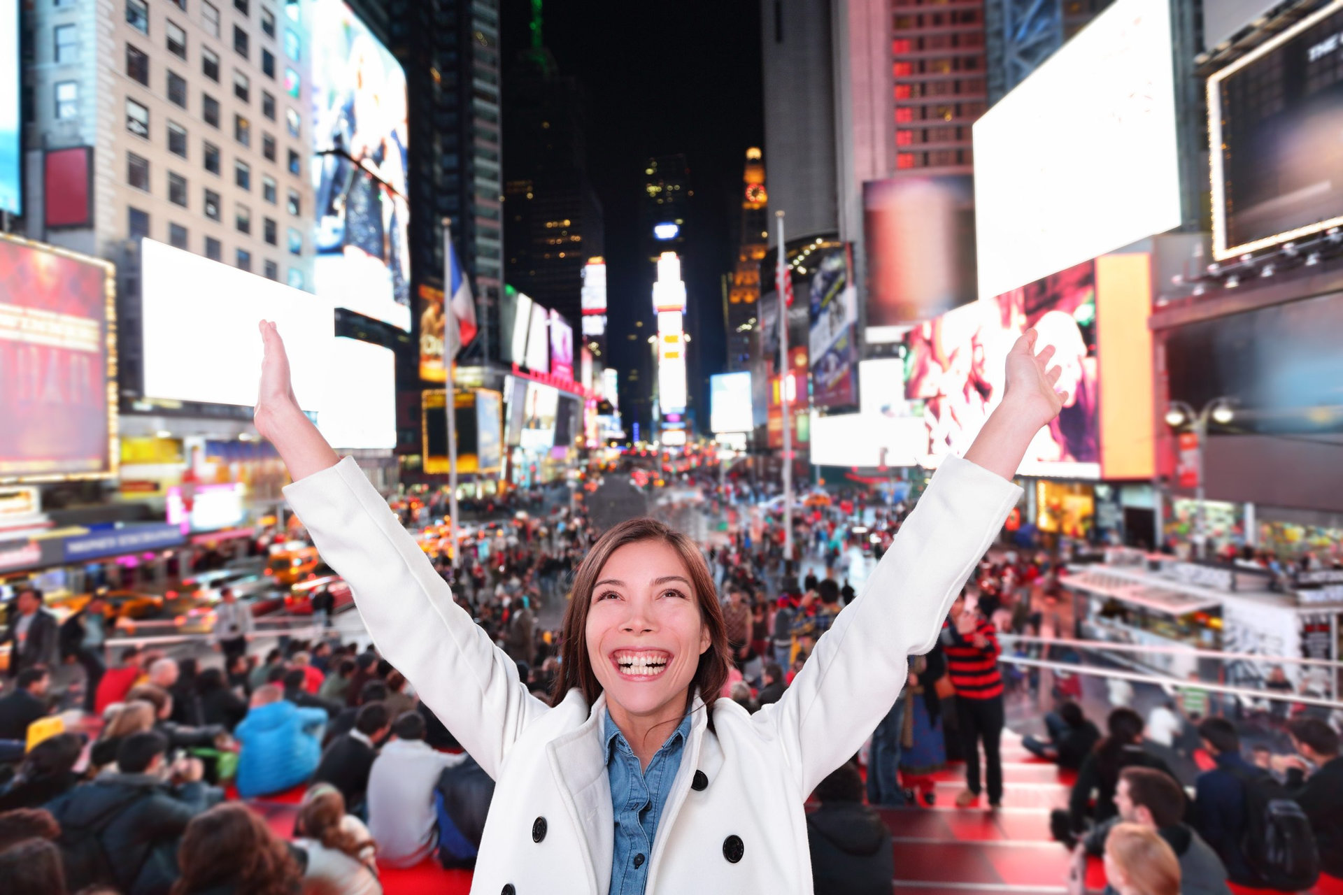 Happy excited woman in New York City, Manhattan, Times Square cheering celebrating joyful at night with arms raised. Smiling cheerful Multiethnic Asian Caucasian young urban professional in her 20s.