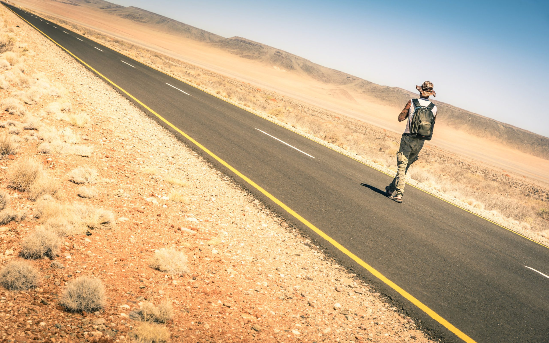 Lonely man walking along the road among the namibian african desert - Concept of alternative lifestyle - Travel trip adventure around the world