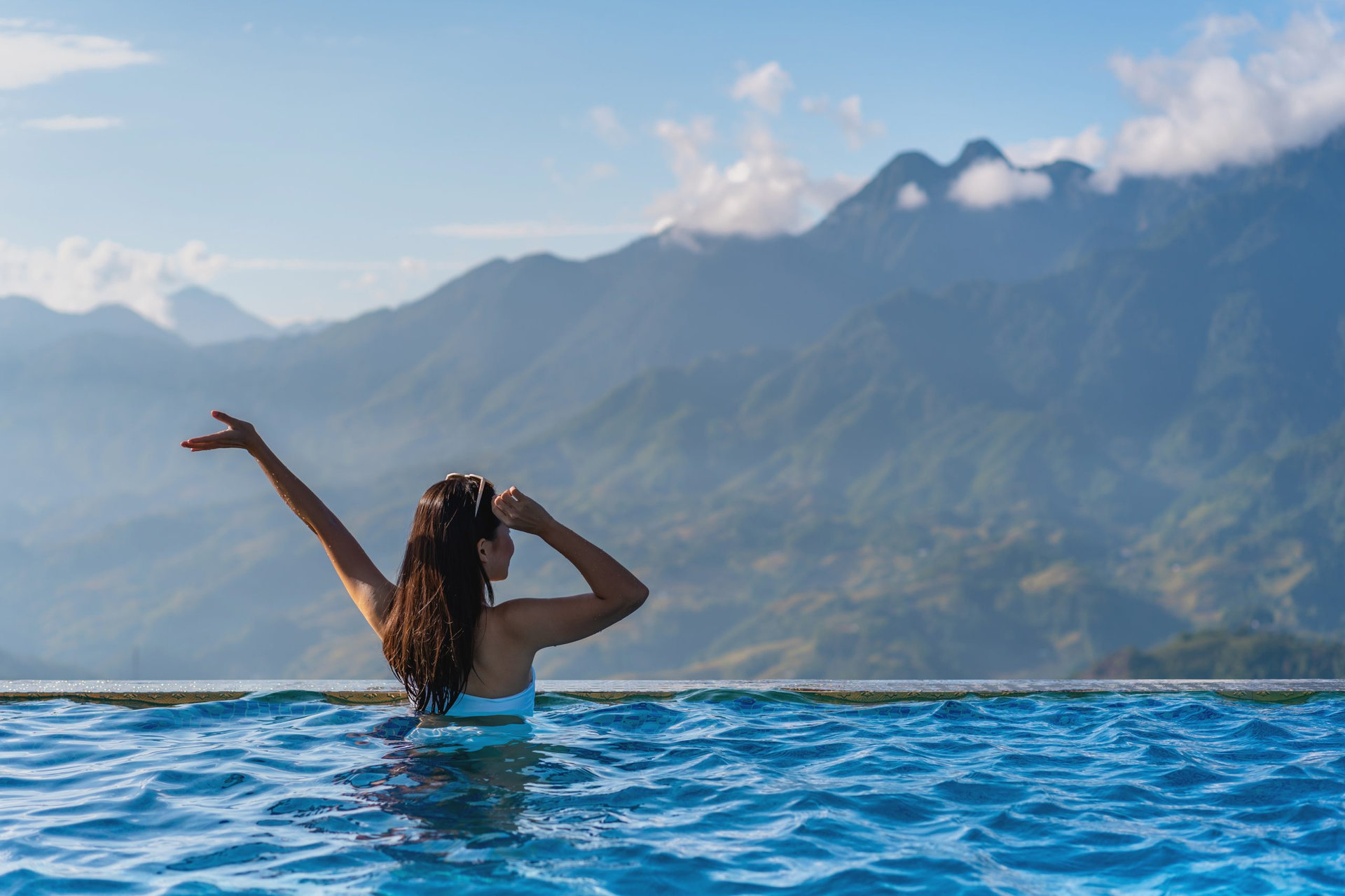 Young woman traveler relaxing in sky pool and looking at the beautiful nature landscape with blue sky and mountains in Sapa, Vietnam