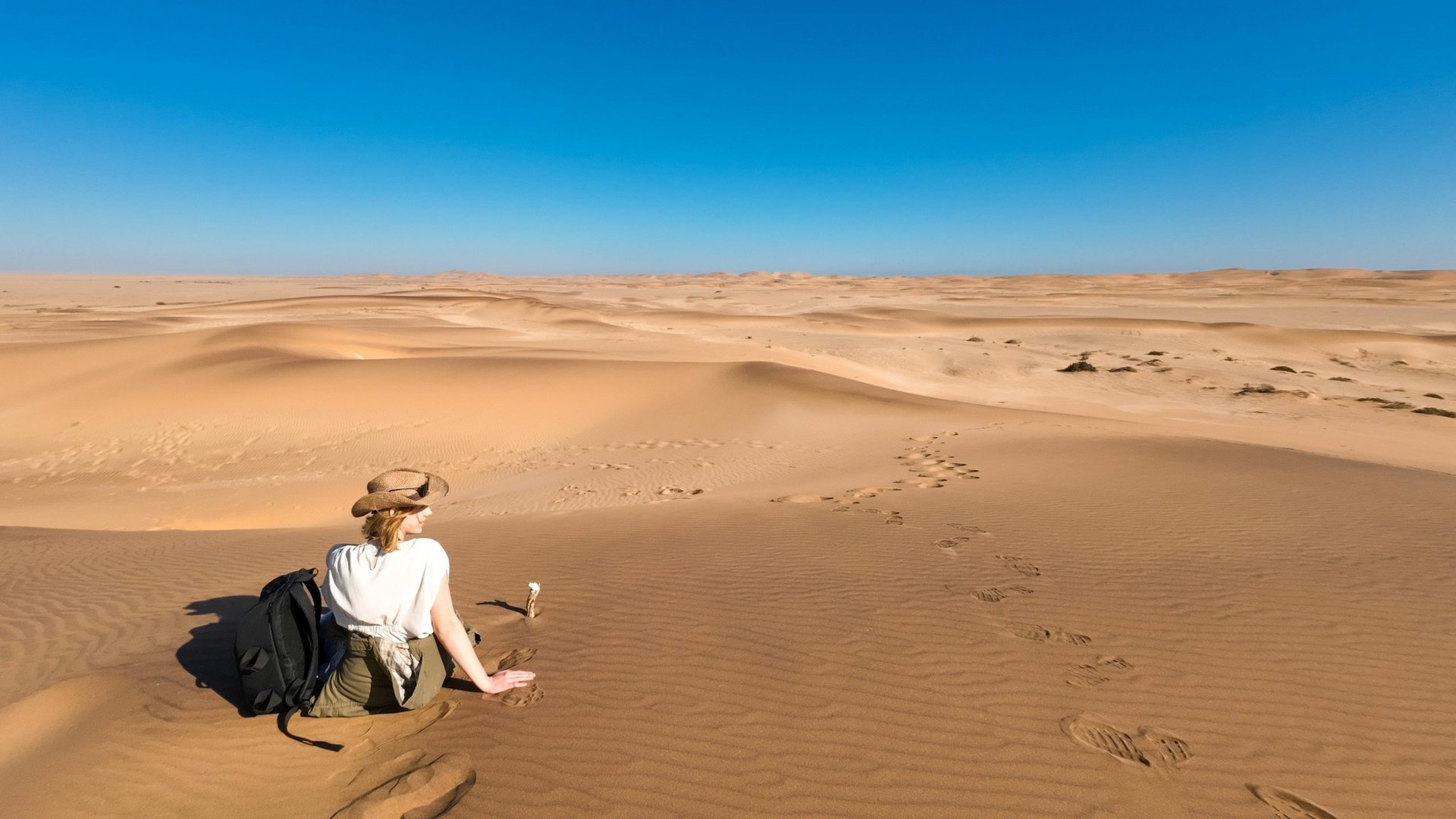 Lone traveler sitting on the sand dunes under a clear blue sky in Namibia, Africa