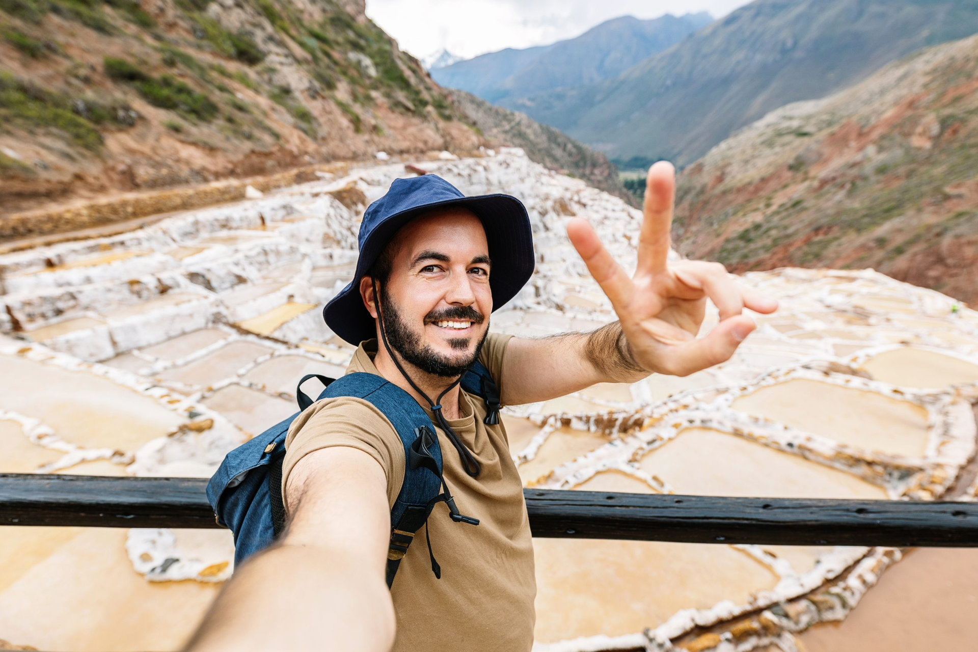 EvotoHappy young traveler man taking selfie portrait while enjoying vacation in Peru. Joyful tourist visiting salt terrace in Maras. Travel and holiday lifestyle concept.
