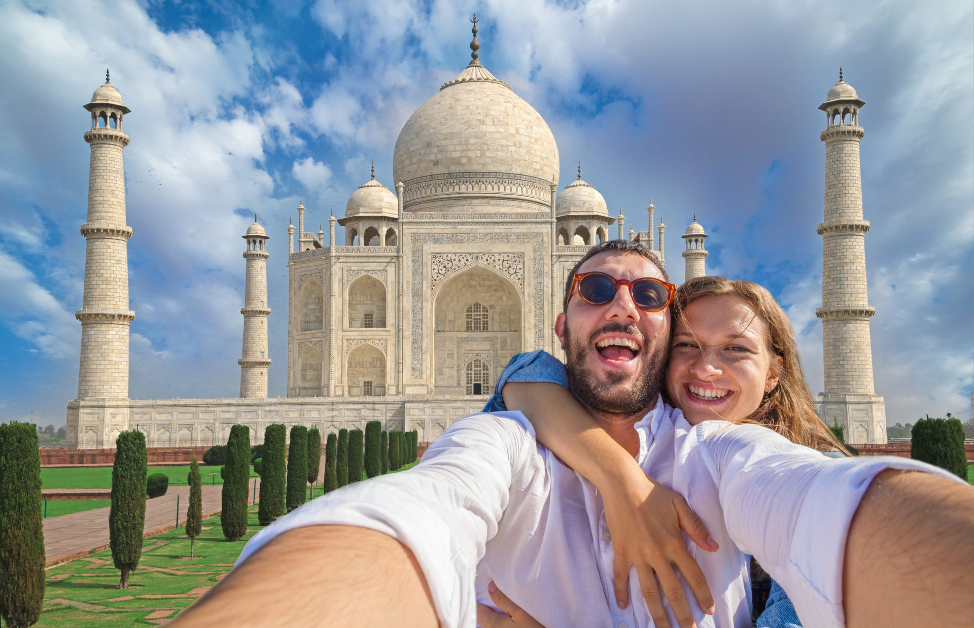 Tourism in India. Handsome couple in love in holiday using mobile phone to take selfie picture at Taj Mahal, Agra, Uttar Pradesh, India